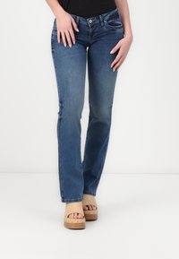 Vaqueros de mezclilla azul oscuro con un diseño de pierna recta, que cuentan con bolsillos frontales y un desvanecimiento sutil, combinados con sandalias de plataforma beige.