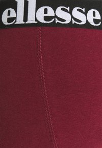 Burgunderfarbene Leggings mit einem schwarzen elastischen Bund, der mit weißem 'ellesse'-Branding versehen ist. Glatte Oberfläche mit sichtbaren Nahtdetails.