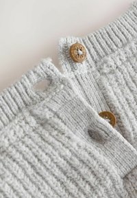 Capo in maglia grigia con texture a coste, dotato di chiusura con grande bottone in color legno naturale e dettaglio a taglio sul colletto.