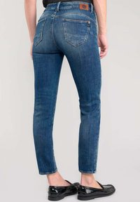 Jean skinny bleu en denim avec une taille mi-haute, un délavage subtil et des poches arrière. Associé à des ballerines noires en cuir verni.