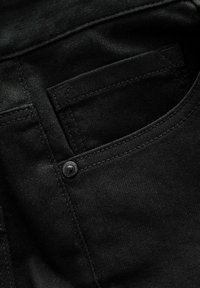 Zwart denim stof met een achterzak met zichtbare stiksels en een zwarte metalen knoop. De textuur lijkt glad en duurzaam.