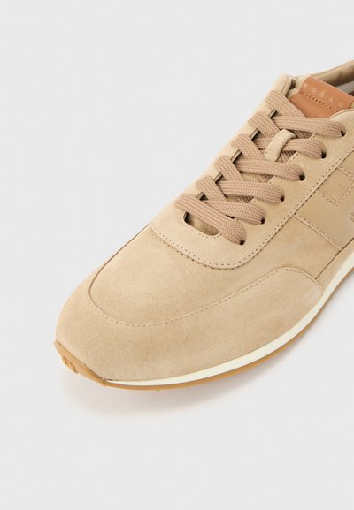 Baskets en daim beige avec lacets assortis, logo latéral ton sur ton, et semelle en caoutchouc blanche avec bande de roulement marron, vues de dessus en angle.