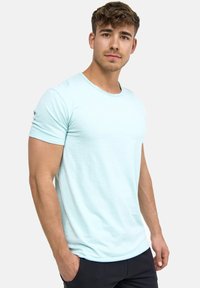 Light blue short-sleeve t-shirt with a crew neck and smooth fabric texture. Model poses with hands in pockets, against a plain background.