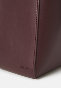 Sac en cuir bordeaux avec une texture lisse, arborant un logo « HVISK » embossé au bas et des lignes de design contemporaines et épurées.