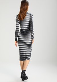 Robe en maille rayée à manches longues, présentant des rayures alternées bleu marine et blanches, coupe ajustée et longueur au genou ; accompagnée de bottines noires.