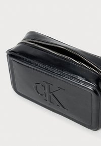 Črna usnjena kozmetična torbica pravokotne oblike, z zadrgo, vtisnjenim logotipom "CK" in gladko teksturo. Podrobnosti z zadrgo iz kovine.