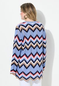 Knittröja med ett blått, brunt, rött och vitt zick-zackmönster, med en scallopad nederkant och öppen design. Strukturerad tyg och långa ärmar.