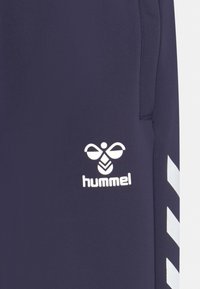 Marinefarbene Sporthose mit weißem Hummel-Logo und Chevron-Akzent an der Seite. Aus weichem, dehnbarem Stoff mit glatter Textur gefertigt.