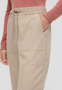 Beige joggingbroeken van een gestructureerde stof, met een elastische tailleband met trekkoord, zijzak en een cargostijlzak.