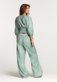 Dvojdielny outfit s priliehavým, smockovaným crop topom a voľnými nohavicami. Upravený v zelenej farbe s ružovými akcentmi, s objemnými rukávmi.
