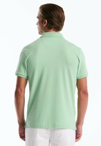 Mintgroene polo met korte mouwen, van een stevige stof met een platte kraag. Bevat zijslits aan de zoom voor extra bewegingsvrijheid.