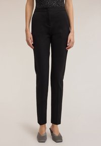 Czarne spodnie o dopasowanym kroju, wąskie, z płaskim przodem i bez widocznych kieszeni. Gładka faktura tkaniny, zestawione z szarymi mule na spiczastym nosku.