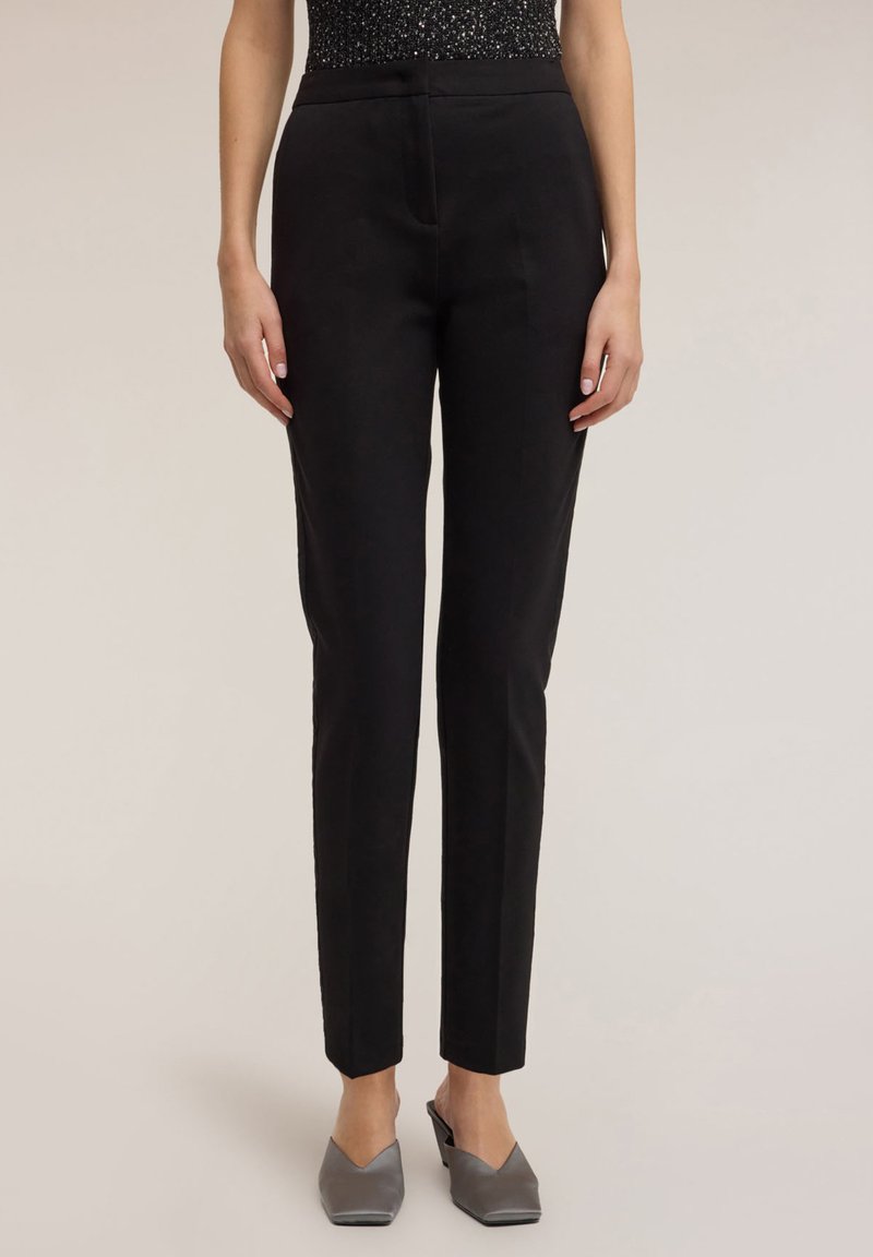 Czarne spodnie o dopasowanym kroju, wąskie, z płaskim przodem i bez widocznych kieszeni. Gładka faktura tkaniny, zestawione z szarymi mule na spiczastym nosku.