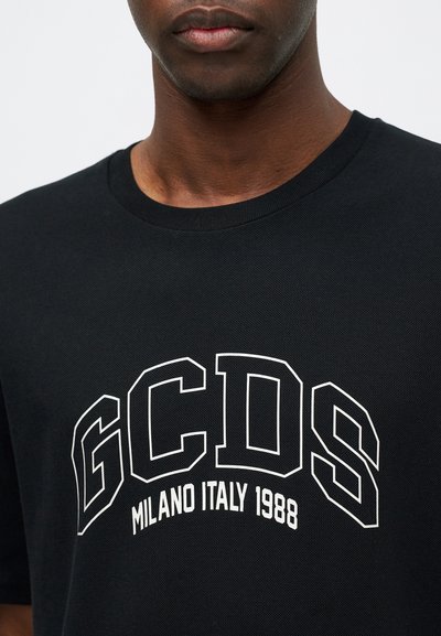 Juodas marškinėliai su apvalia iškirpte ir tekstūruotu audiniu. Priekyje yra balti užrašai: "GCDS MILANO ITALY 1988" ryškiu sportiniu šriftu.