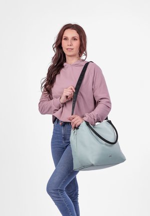Light blue shoulder bag made of smooth material, featuring black accents and a logo. Model wears a pink hoodie and blue jeans.