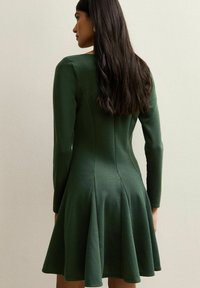 Ciemnozielona sukienka z długim rękawem i rozkloszowanym dołem. Miękka tkanina, dopasowana góra i plisowane detale z tyłu. Proste, czyste linie.