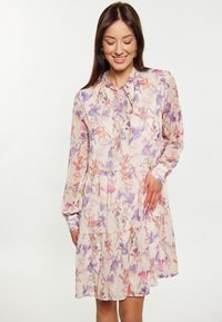 Blumenkleid in hellem Beige mit lila und orangefarbenen Mustern, das einen gebundenen Kragen, lange Ärmel und einen gestuften Rüschensaum hat. Halbtransparente Stoffqualität.