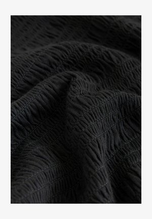 Čierna textúrovaná tkanina s pokrčeným vzorom, obsahujúca vystúpené čiary a jemný lesk. Mäkký a tkaný materiál s viditeľnými švovými detailmi.