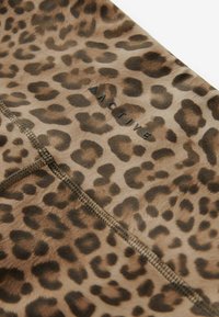 Tela de estampado de leopardo con una textura suave y manchas marrón oscuro sobre un fondo color canela. Incluye una costura y un detalle de logo en negro.