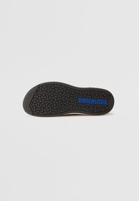 Black rubber outsole with a wavy tread pattern and blue "BIRKENSTOCK" logo, featuring a rounded shape and textured surface.