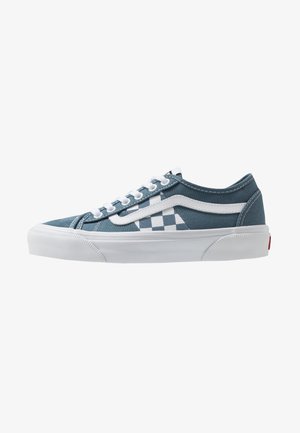 Niskie niebieskie sneakersy z białym wzorem w kratkę, białymi sznurowadłami, białym bocznym paskiem i grubą białą gumową podeszwą.