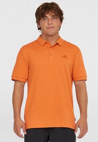 Polo tričko s krátkym rukávom v jasne oranžovej farbe, vyrobené z texturovanej tkaniny. Obsahuje klasický golier a vyšívané logo na hrudi.