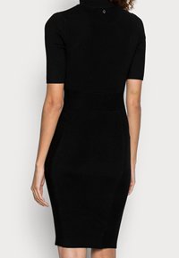 Černé žebrované pletené šaty s krátkými rukávy a vysokým límcem. Hladce padnoucí silueta s texturovanými detaily a středně dlouhým lemem vzadu.