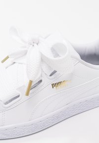 Baskets Puma Basket blanches avec de gros lacets blancs noués en nœud, détail du logo doré et semelle en caoutchouc texturée.