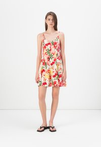 Abito floreale con scollo a V, spalline sottili e gonna svasata. Presenta fiori rossi, rosa e gialli su uno sfondo chiaro. Indossato con sandali neri.