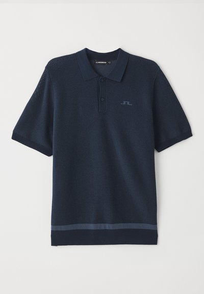 Camisa polo azul marino con un tejido texturizado, mangas cortas, tapa botones y un logotipo sutil en el pecho. Presenta un ribete contrastante en la parte inferior.