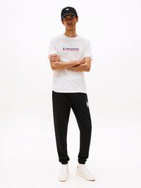 Weißes Baumwoll-T-Shirt mit "Tommy Jeans"-Logo, schwarze Trainingshose und weiße Sneaker. Die Kappe ist schwarz mit einem Logopatch. Lässiger Schnitt.