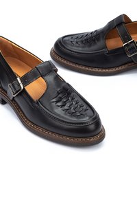 Zwarte leren schoenen met een geweven ontwerp op de neus, een gesp-sluiting en een bruine zool. Gladde textuur met een contrasterende kleur aan de binnenkant.