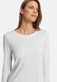 Světle modrý top s dlouhými rukávy a kulatým výstřihem. Hladká tkanina s minimem švů a přiléhavým střihem. Čistá a jednoduchá estetika.