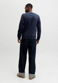 Námořnická modrá mikina s kulatým výstřihem, v kombinaci s tmavými denimovými džíny s ohrnutým lemem. Oblečení doplňují béžové boty.