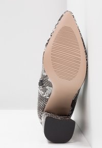 Chaussure à bout pointu imprimée serpent noir et blanc. Dispose d'une semelle lisse avec une traction texturée et d'un talon bloc pour la stabilité. Détail de fermeture éclair latérale.