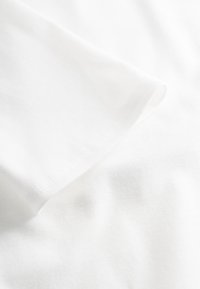 Weißer Baumwoll-T-Shirt-Stoff mit glatter Oberfläche und einem umgefalteten Ärmel. Verfügt über eine saubere Kante mit dezenten Nähten.