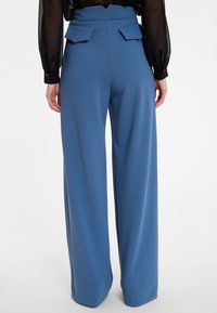 Blauwe wijde pantalon met een gladde textuur, hoge taille en twee platte achterzakken. Het materiaal lijkt zacht en zorgvuldig afgewerkt.