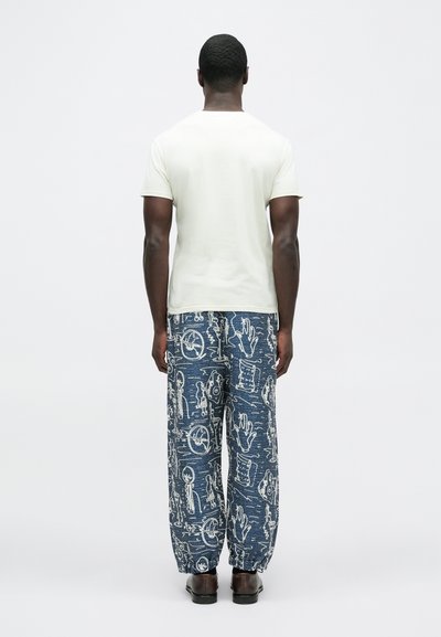 Ανοιχτό μπεζ κοντομάνικο μπ λουζάκι με στρογγυλή λαιμόκοψη, συνδυασμένο με σκούρο μπλε παντελόνι με σχέδιο και κορδόνι στη μέση, που διαθέτει λευκά γραφικά σχέδια.