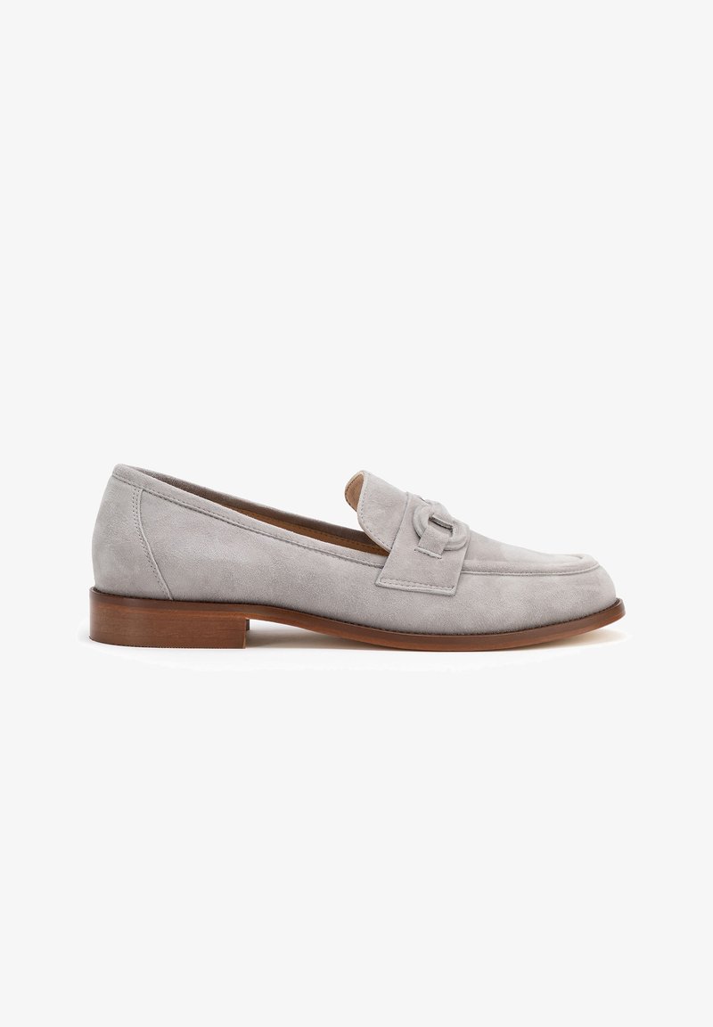 Mocassino in suede grigio chiaro con suola piatta marrone, caratterizzato da una striscia decorativa sulla parte superiore e un design a punta arrotondata.