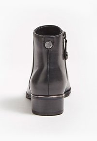 Bottine en cuir noir avec un petit talon empilé, une fermeture éclair latérale et un emblème métallique rond décoratif sur la languette arrière.