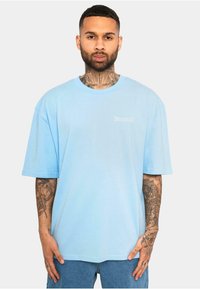 T-shirt oversized de culoare albastru deschis, realizat dintr-un material moale, cu mâneci scurte, având un mic logo alb pe piept și un decolteu rotund.