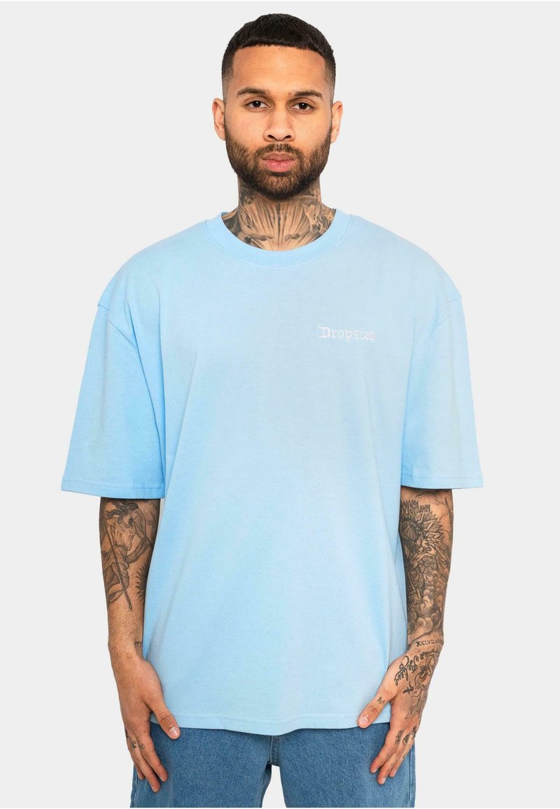 T-shirt oversized de culoare albastru deschis, realizat dintr-un material moale, cu mâneci scurte, având un mic logo alb pe piept și un decolteu rotund.