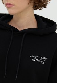 Felpa nera realizzata in cotone con una consistenza morbida, dotata di una tasca frontale e una frase ricamata in bianco "NEWER FINISH ANYTHING" sul petto.