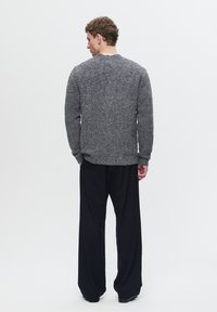 Grå strikket sweater med en tekstureret overflade, rund hals og lange ærmer, kombineret med løse sorte bukser. Outfittet viser en afslappet pasform.
