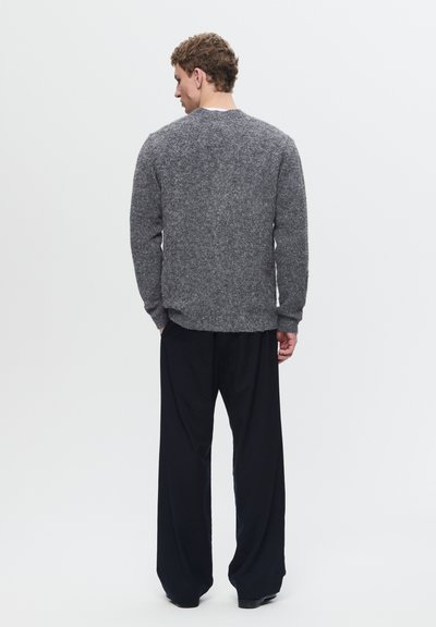 Grijze gebreide trui met een textuurafwerking, ronde hals en lange mouwen, gecombineerd met losse zwarte broek. De outfit heeft een casual pasvorm.