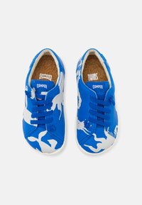 Un paio di scarpe da ginnastica per bambini blu e bianche con design a lacci, suole in sughero e marchio "Camper" sulla linguetta e all'interno del tallone.