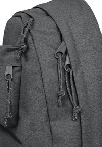 Gray fabric backpack with smooth texture, featuring two drawstring closures and knotted accents. Minimalist design with subtle stitching details.