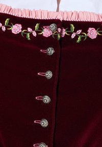 Burgundy sametti vaate, jossa on vaaleanpunaiset röyhelökoristeet, koristeltu kukka-arkkitehtuurilla ja metallinapeilla etuosan sulkemisessa.