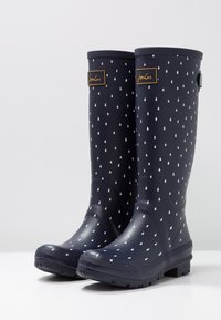 Bottes de pluie bleu marine avec un motif de gouttes de pluie blanches et des patches logo à l'avant, semelles robustes et sangles latérales ajustables.