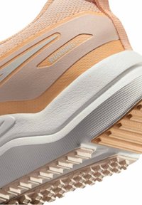 Primer plano de la suela de un zapato de correr en tonos melocotón y blanco con una banda de rodadura texturizada y texto "RUNNING" en el panel lateral.